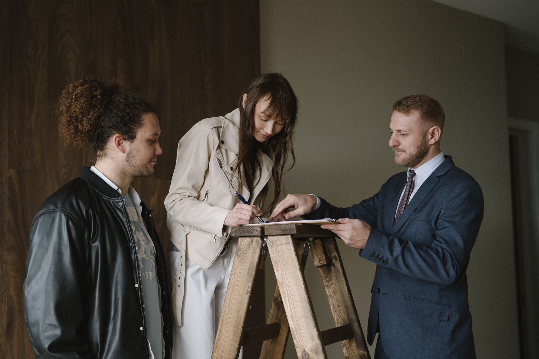 Buyer signing closing documents at real estate transaction with agent and paperwork on table