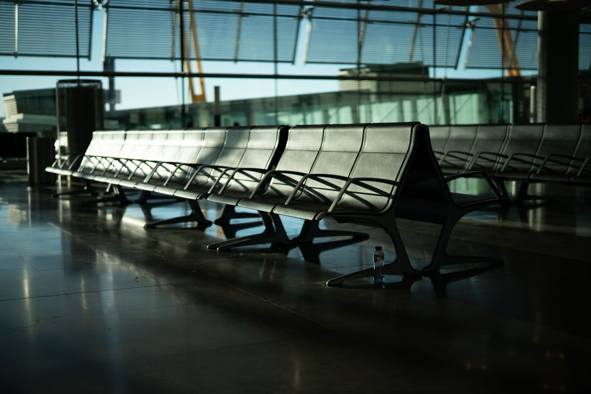 Deserted airport seating area with sunlight streaming through large windows. Calm and quiet atmosphere.