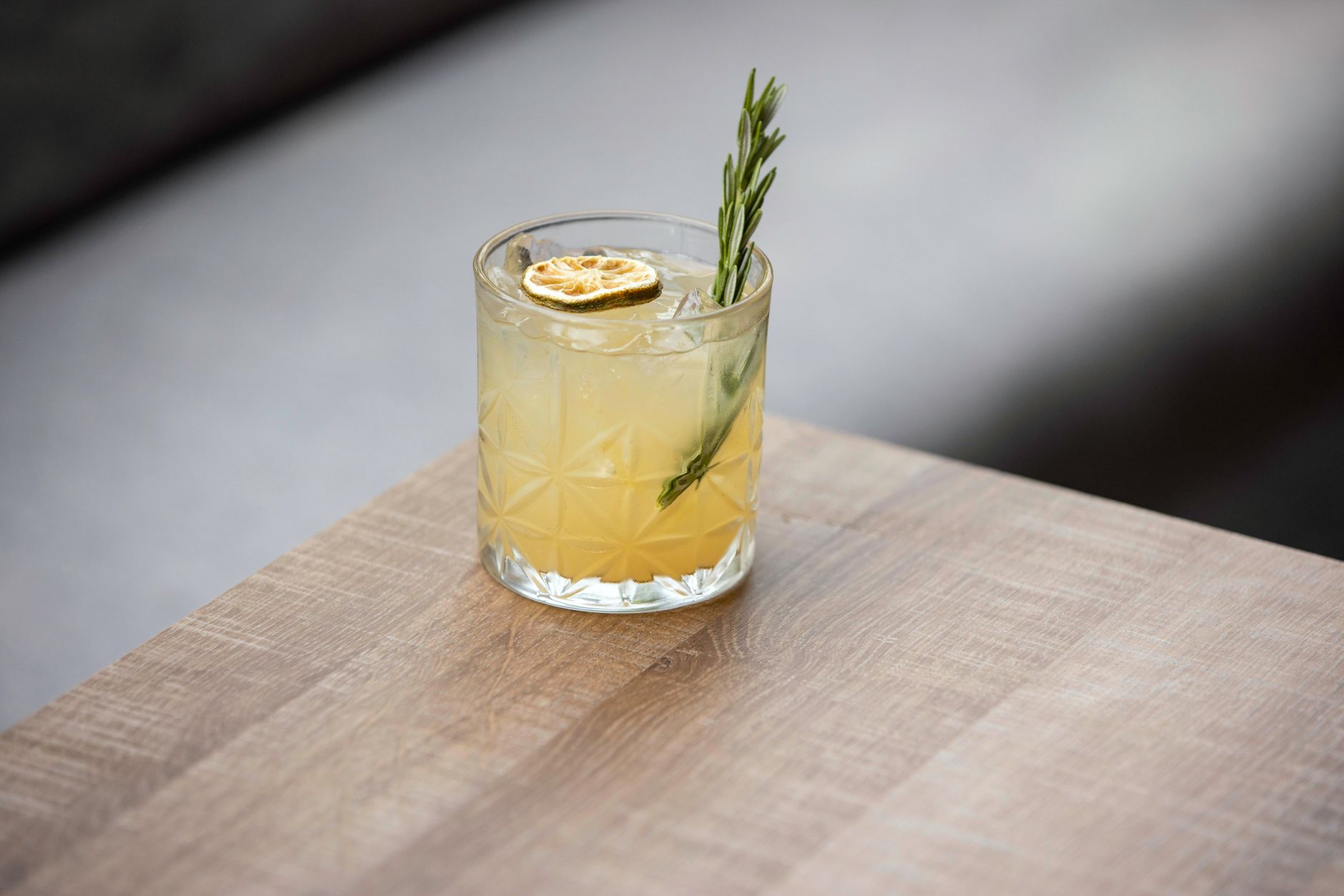 A citrus cocktail garnished with a dried citrus slice and rosemary on a wooden table.