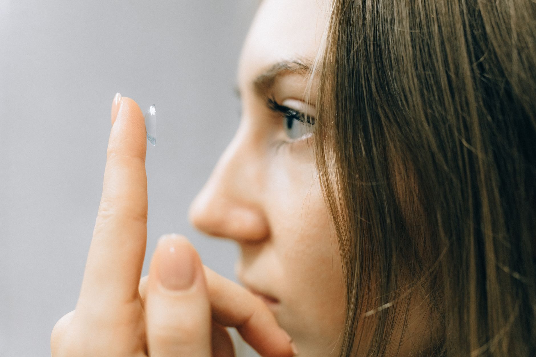 Young woman carefully inserting a colored contact lens into her eye with proper technique and hygiene