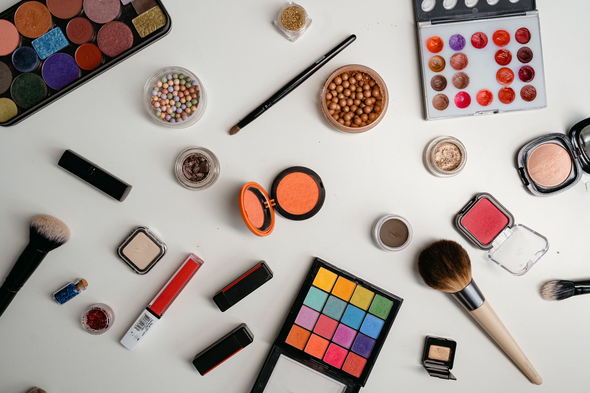 A vibrant collection of makeup and beauty products arranged in a flat lay on a white background.