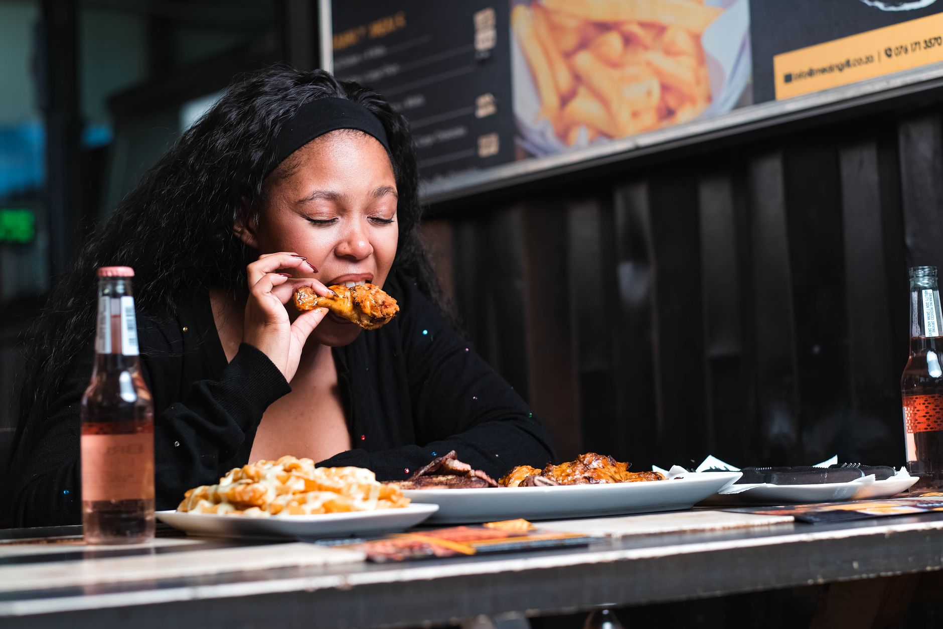 A young woman enjoying a chicken meal at a restaurant, accompanied by drinks and fries.