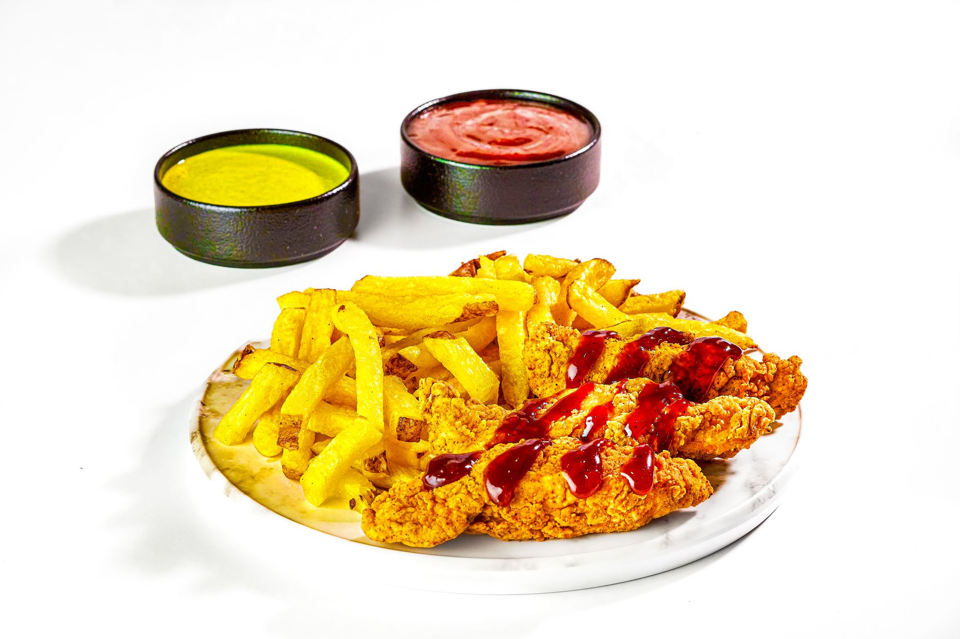 Delicious crispy chicken tenders served with fries and two dipping sauces on a white background.
