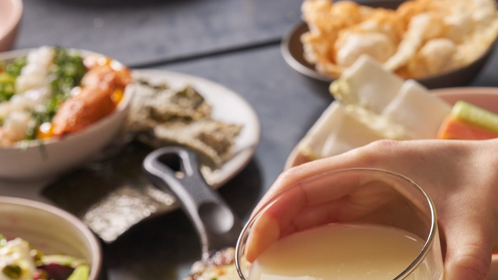 Two hands raising glasses of makgeolli and red wine across a table at 8282