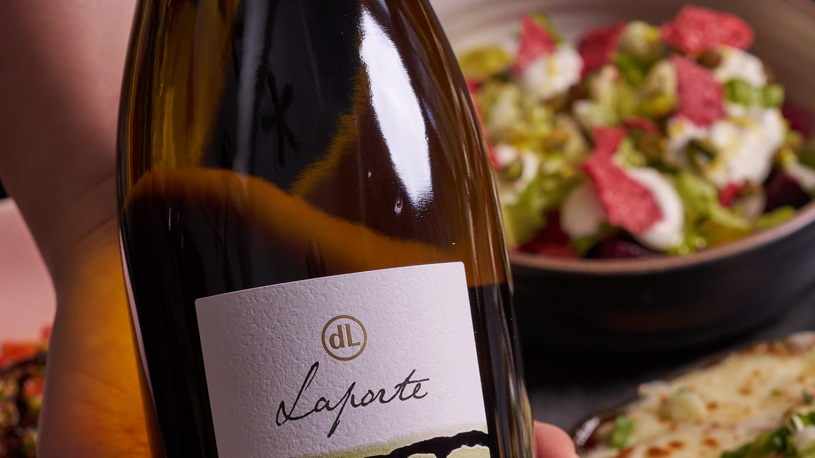 Bottle of white wine held above a table of shared dishes at 8282