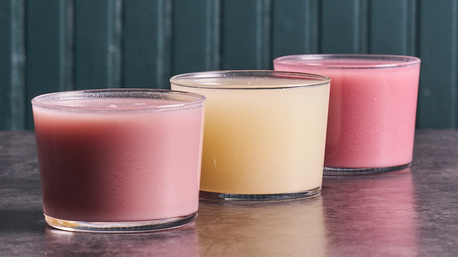 Row of coloured makgeolli drinks in glasses against a teal wall at 8282